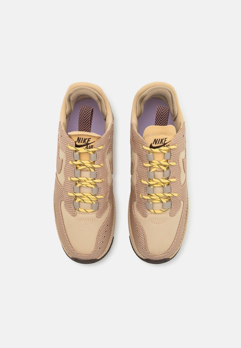 Sneaker Nike Air beige realizzati in materiali mesh e suede, con accenti testurizzati, lacci gialli e una linguetta a motivi. Suola piatta in gomma.