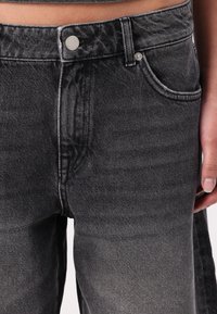 Black denim jeans featuring a high waist, a classic five-pocket design, and subtle fading for texture. Front button closure and area seam details.