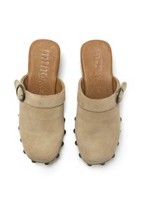 Zuecos de ante beige con una plantilla de cuero marrón, que cuentan con un hebilla lateral y una suela texturizada con remaches redondeados para mayor agarre.
