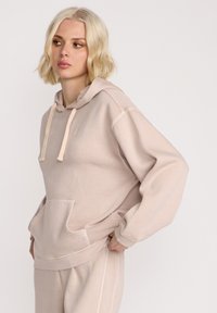 Lys beige hoodie lavet af blød stof, med en forlomme, snøre i hætten og ribbede manchetter, med et afslappet fit design.