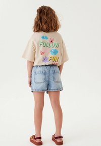 Beige t-shirt med kort ärm och färggrafik "Follow the Fun" samt lekfulla former på baksidan. I kombination med jeansshorts och sandaler.