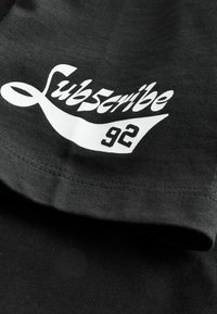 T-shirt nero a maniche corte con grafica bianca che presenta il testo "Subscribe" e il numero "92" in un font audace e informale sul davanti.