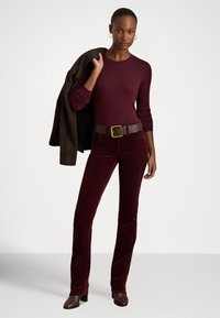 Bordový priliehavý sveter v kombinácii s kordurovými nohavicami rovnakej farby. Hnedý kožený opasok so zlatou prackou, doplnený tmavým kockovaným sakom prehodeným cez jedno rameno.