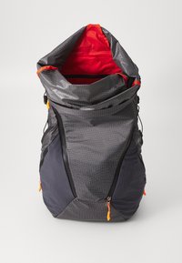 Sac à dos avec un motif de grille gris, un intérieur rouge et des fermetures éclair orange. Il dispose d'une fermeture enroulable et de sangles ajustables sur les côtés.