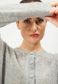 Ljusgrått stickat cardigan med en texturerad, mönstrad design. Har tre knappar fram och ribbade ärmar. Sidenliknande utseende.