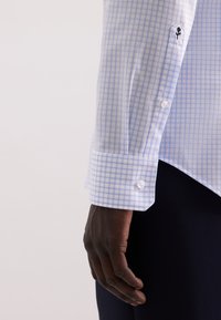 Hemelsblauw en wit geblokt overhemd met een strakke kraag en gestikt bloemen detail op de manchetten. Glad materiaal, getailleerde pasvorm.