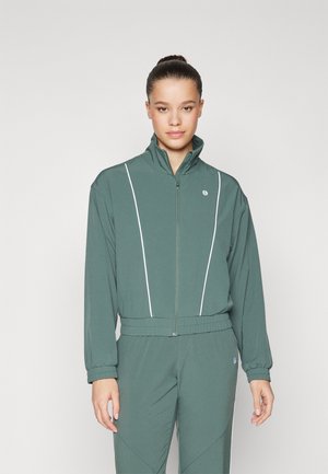 Grön zip-up jacka med vita accentstrimmor, långa ärmar och hög krage; bärs tillsammans med matchande byxor i mjukt, slätt tyg.