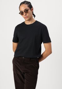 Svart t-shirt med kort ärm och rund halsringning, kombinerad med mörkbruna corduroybyxor med framknapp och fickor.