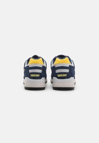 Navy blue suede sneakers with yellow accents and mesh detailing. Features a cushioned sole and prominent “SAUCONY” branding on the heel.