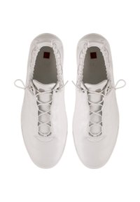 Para białych skórzanych sneakersów wsuwanych z elastycznymi krawędziami i krzyżującymi się sznurówkami, podpatrzona z góry.
