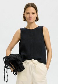 Czarny lniany top bez rękawów z okrągłym dekoltem, zestawiony z kremowymi spodniami z troczkami i czarną szydełkowaną torbą. Gładka tekstura, casualowy styl.