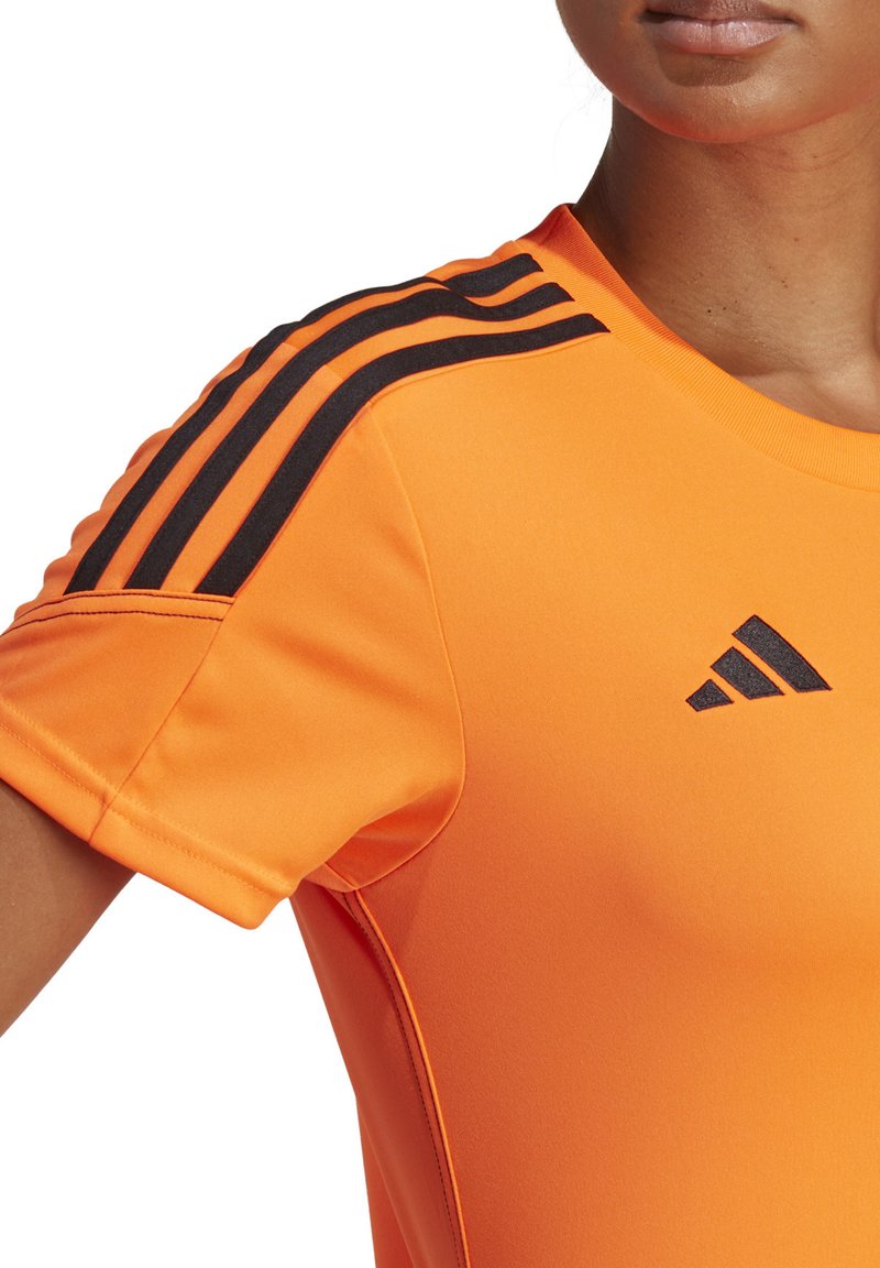 Oranje sportshirt met korte mouwen, met zwarte drie-strepen details op de schouders en een zwart Adidas-logo op de borst.