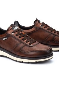 Zapatillas de cuero marrón con un acabado texturizado, punta redonda y cordones marrones. Presentan una entresuela blanca y un forro interior negro.