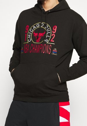 Czarna bluza z kapturem z napisem i logo „Chicago Bulls 1991 1992 NBA Champions”, noszona przez osobę z rękami w przedniej kieszeni.