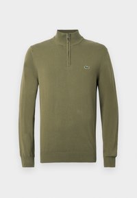 Maglione verde oliva a maniche lunghe con colletto zip a un quarto e piccolo logo di coccodrillo sul lato sinistro del petto.