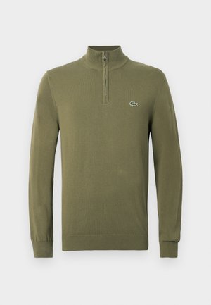 Olivovo zelený sveter s dlhým rukávom, s zipsom na štvrtinu goliera a malým logom krokodíla na ľavej hrudi.