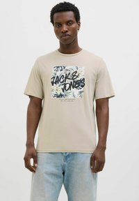 Camiseta de color beige claro con cuello redondo, que presenta un estampado gráfico de hojas tropicales y el texto "JACK & JONES" en letras negritas negras.
