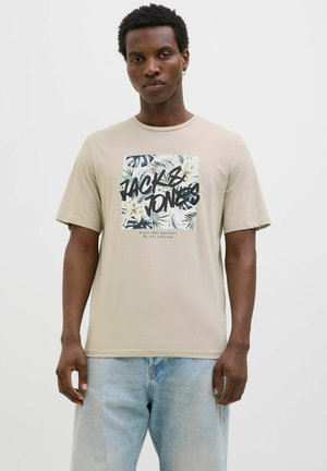 Camiseta de color beige claro con cuello redondo, que presenta un estampado gráfico de hojas tropicales y el texto "JACK & JONES" en letras negritas negras.