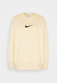 Ljusgul Nike-tröja med långa ärmar, rundad halsringning och en svart logotyp på bröstet. Slät textur och avslappnad passform.
