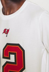 Bílý bavlněný tričko s velkým červeným číslem "2" obtaženým černou a oranžovou barvou, s malým logem Buccaneers nad číslem.
