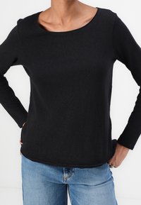 Svart långärmad topp i mjuk bomull, med rund halsringning och avslappnad passform, kombinerad med blå denimjeans.