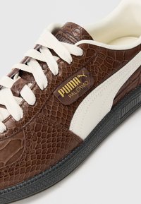 Smeđe puma tenisice s gornjim dijelom od teksturirane zmijske kože, kremastim vezicama, bijelim bočnim prugama i crnom gumiranom potplatu s detaljima logotipa.