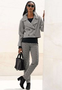 Graue doppelreihige Jacke, schwarzes geripptes Oberteil, gestreifte schwarz-weiße Hose, schwarze Handtasche und Stiefeletten. Große Sonnenbrille und creolenförmige Ohrringe.