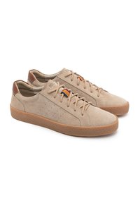 Baskets en daim beige avec une semelle en caoutchouc texturé, présentant des perforations sur le côté et un patch arrière en cuir marron avec des accents colorés.