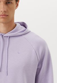 Lys lilla hettegenser med kengurulomme og justerbare snorene. Har en subtil Nike-logo brodert på brystet. Myk tekstur.