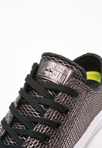 Baskets en mesh noir avec motif texturé, lacets noirs et œillets métalliques. Comprend une languette argentée brandée sur la languette et un intérieur jaune.