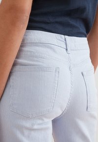 Jeans a righe blu chiaro con una superficie liscia, vita aderente e due tasche posteriori. La cintura è leggermente più alta per una vestibilità sicura.
