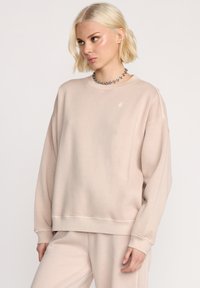Beżowa, oversize bluza z okrągłym dekoltem, długimi rękawami i ściągaczami. Posiada subtelne logo na klatce piersiowej oraz miękką, strukturalną tkaninę.