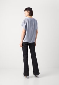 Haut bleu clair à manches courtes avec une coupe décontractée et un tissu texturé, associé à un jean évasé noir et des chaussures à talons carrés transparentes.