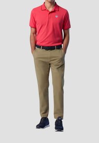 Polo shirt rosso con colletto a contrasto, pantaloni khaki e scarpe da ginnastica nere. Include un logo sul lato sinistro della maglietta.