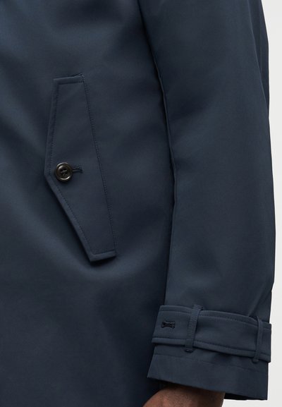 Ναυτικό παλτό με λεία υφή, κεκλιμένη πλαϊνή τσέπη με κουμπί και ρυθμιζόμενο μανσέτα με λεπτομέρεια λουριού.