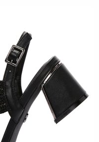 Sandalo nero con un tacco largo e massiccio, in materiale di pelle, cinturino alla caviglia regolabile con fibbia in argento e design superiore testurizzato.
