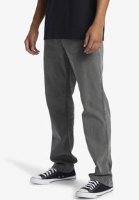 Gray denim jeans with a straight fit, featuring a faded wash and side stitching. Paired with black low-top sneakers with white accents.