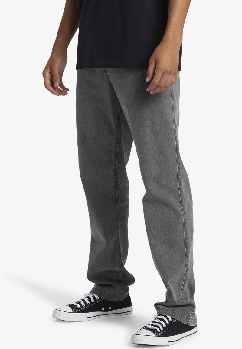 Gray denim jeans with a straight fit, featuring a faded wash and side stitching. Paired with black low-top sneakers with white accents.