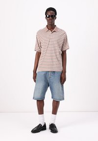 Stribet brun og creme polo skjorte med krave, parret med lyseblå denimshorts. Sorte solbriller og sorte loafers supplerer outfittet.