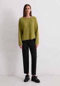Gebreide trui in lichtgroen met een brede halslijn, gedragen met zwarte tapse broek en zwarte veterschoenen. Glad textuur, ontspannen pasvorm.