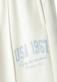 White sweatshirt featuring textured fabric, with light blue printed text reading "USA 1967" and "Enjoy the moment MEMORIES" in varying fonts.