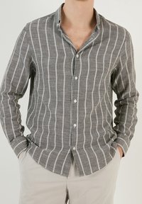 Grijze button-up shirt met witte verticale strepen, gemaakt van textuurstof. Beschikt over een kraag, lange mouwen en een standaard knoopsluiting.