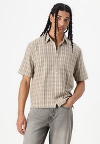 Camicia a maniche corte con motivo a quadri in tonalità beige, dotata di colletto button-down e tessuto leggero. Texture liscia con una vestibilità rilassata.