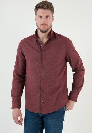 Burgundi gombos ing textúrált anyagból, hosszú ujjakkal és hegyes gallérral. Fekete gombokkal és ívelt szegéllyel rendelkezik.