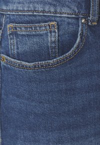 Denim fabric in deep blue with contrasting gold stitching. Features a small back pocket, slightly faded texture, and smooth finish.