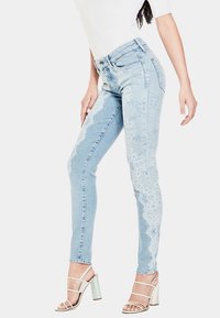 Vaqueros de denim azul claro con detalle de encaje a lo largo del costado, diseño de cintura alta y ajuste slim. Combinados con tacones plateados con tiras.