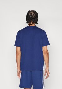 T-shirt en coton bleu marine à manches courtes, avec un col rond et une coupe décontractée, présentant des coutures visibles, porté avec un short assorti.