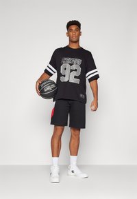 Black short-sleeve shirt with "CHAMPION 92" print and white stripes, paired with black shorts featuring a red accent, and white sports shoes.