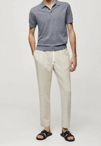 Polo shirt en tricot gris charbon à manches courtes, associé à un pantalon beige clair à cordon de serrage et des sandales noires. Texture lisse et coupe ajustée.