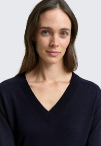 Granatowy sweter dziany z dekoltem w serek, z prążkowanym wykończeniem przy szyi i szwach na ramionach, charakteryzujący się miękką fakturą i dopasowanym krojem.